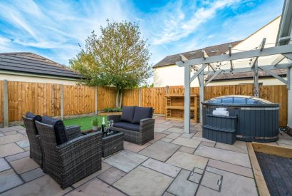 The enclosed garden with a rattan furniture set and a wood-fired hot tub at Pilgrim Cottage, Cheshire