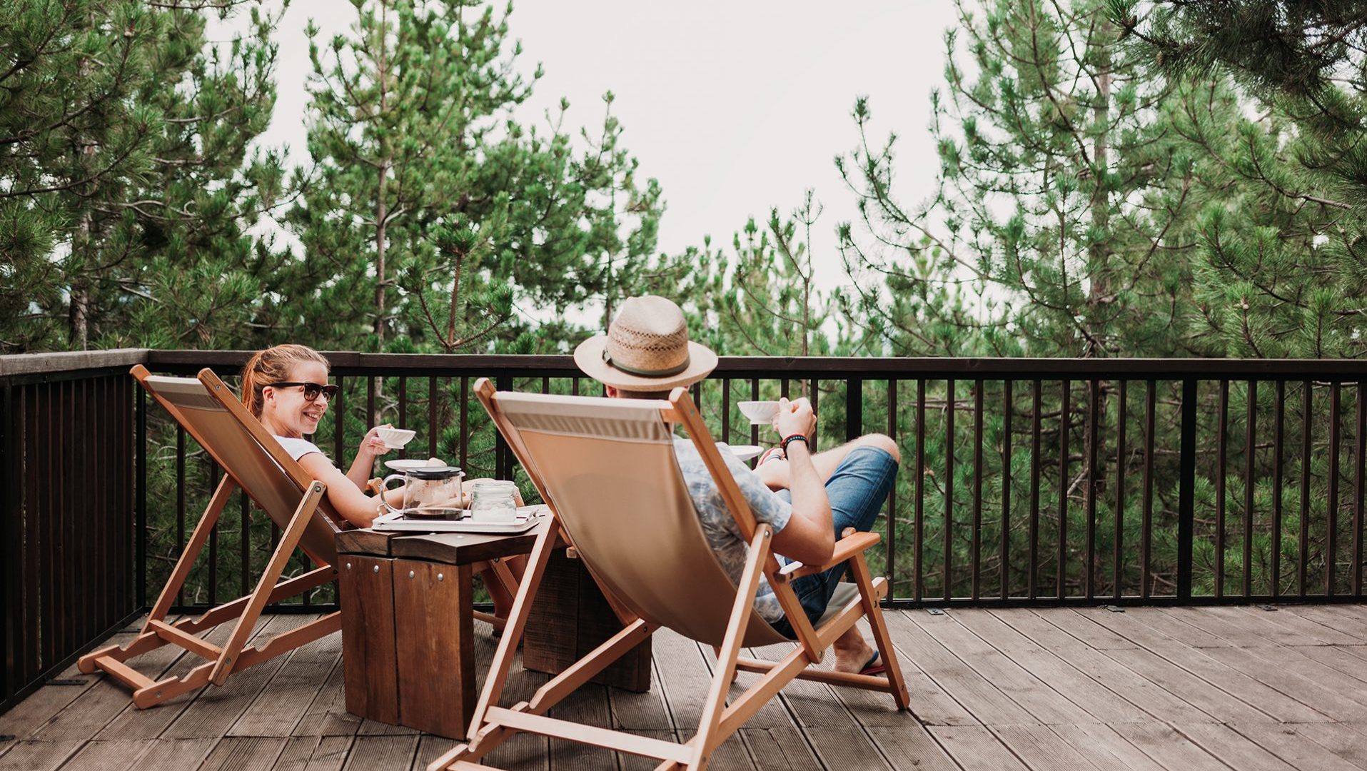 two people sat on deck chairs on a balcony drinking coffee
