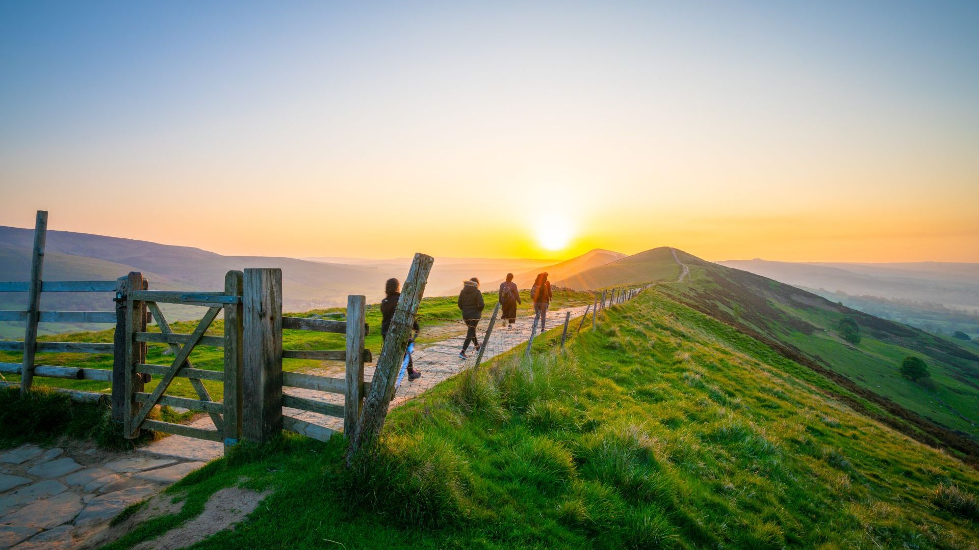 People walking at sunrise over the Great Ridge At Mam Tor Hill In The Peak District