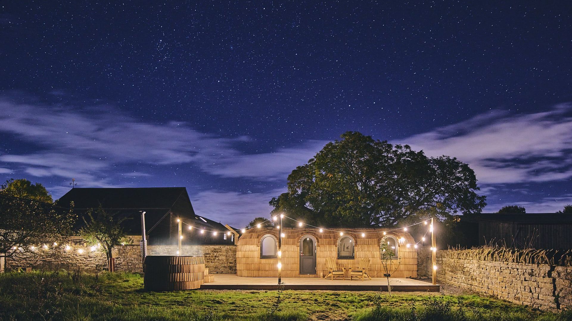The outside of Orchard Snug in Somerset in the evening with hot tub and festoon lights