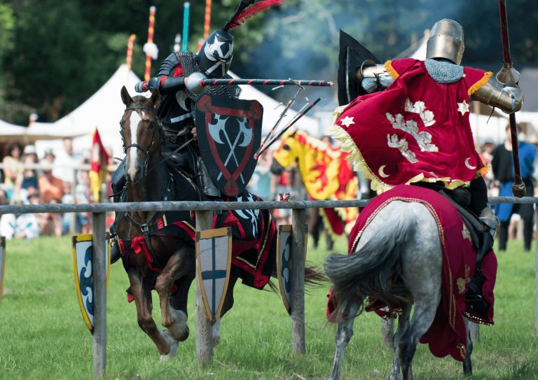 Two people on horseback jousting at an open air event