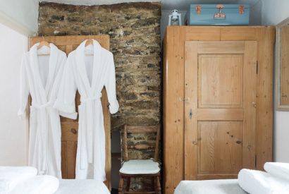 A twin bedroom with two robes handing on the door at Hempston Cottage, Devon