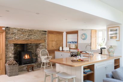 The kitchen with a stone fireplace and log burner at Hempston Cottage, Devon