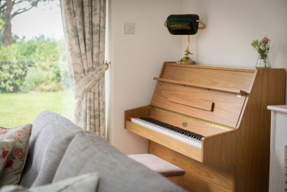 The living room with a piano overlooking the garden at Hempston Cottage, Devon