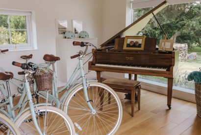 A social space with a grand piano and two bikes overlooking the garden at Brickworks and Vines, Isle of Wight