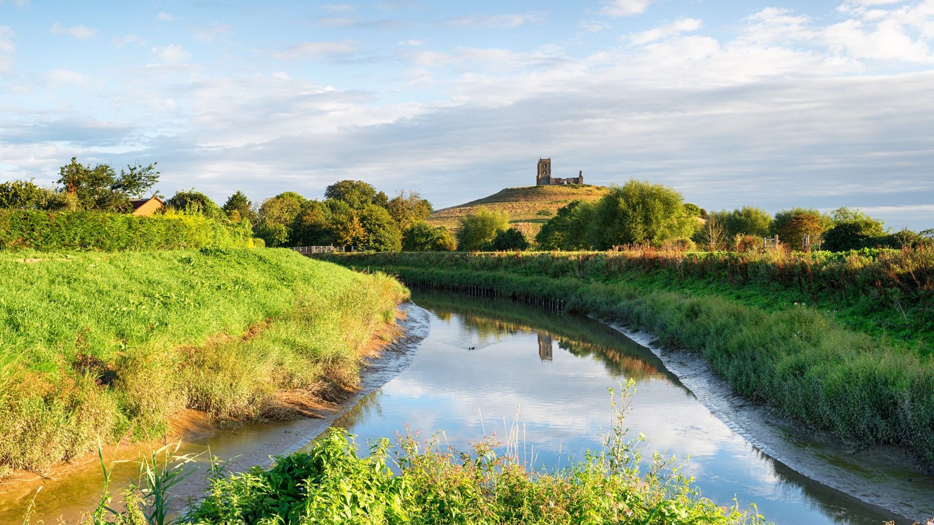 Flat ground of the Somerset Levels wetlands with Burrow Mump hill with monument on it in the distance