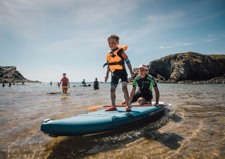 A young boy enjoying a paddle boarding lesson in the sea at Anglesey on a summer day