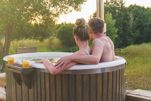 Young couple in an outdoor hot tub gazing at the countryside scenery