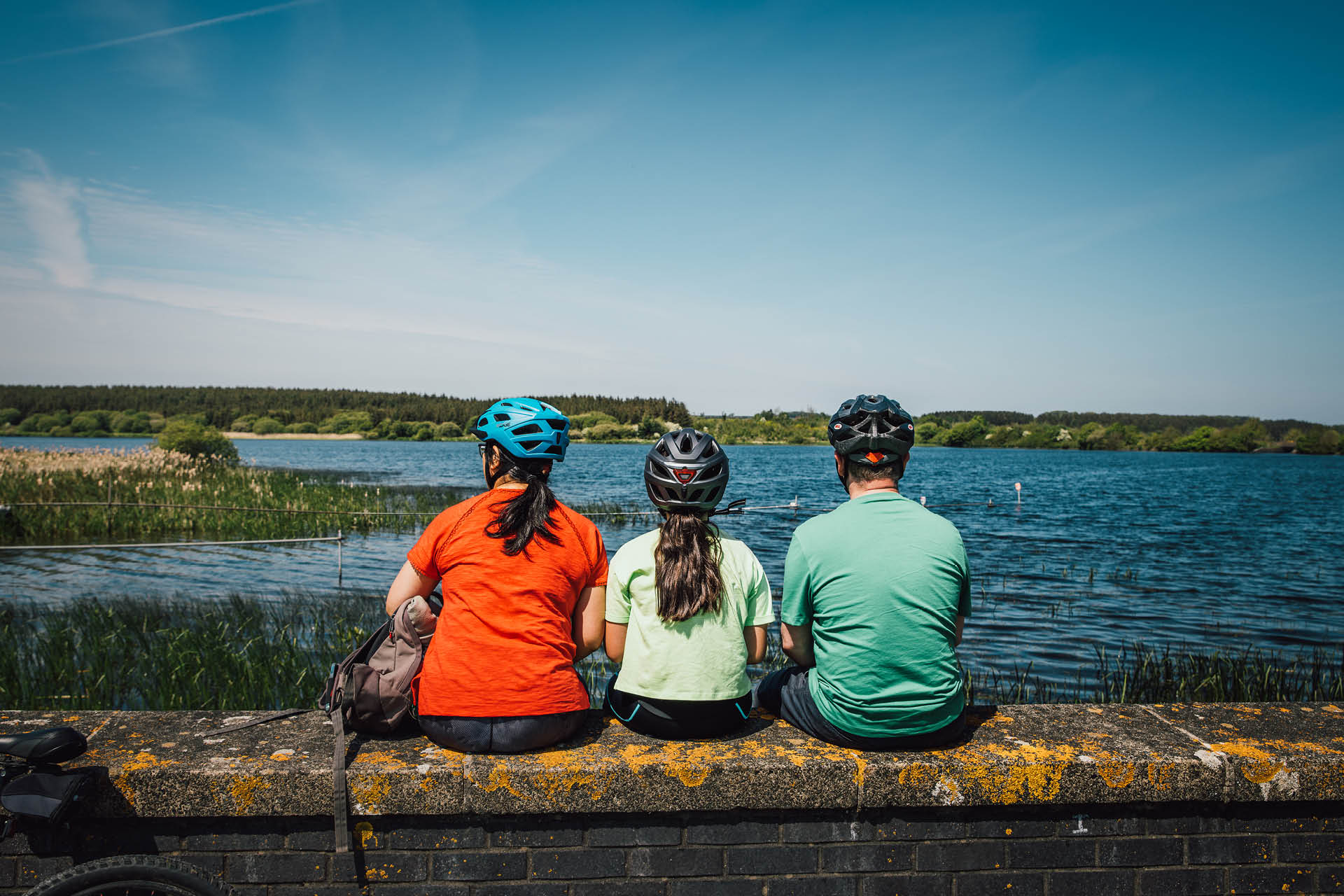 Group of three sitting on a wall overlooking the Anglesey coastline during a bike ride
