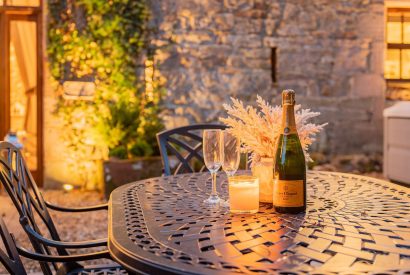 The outdoor dining table with a bottle of champagne and two glasses The private patio at night with a hot tub and a dining table and chairs at Rose Walls, Lake District 