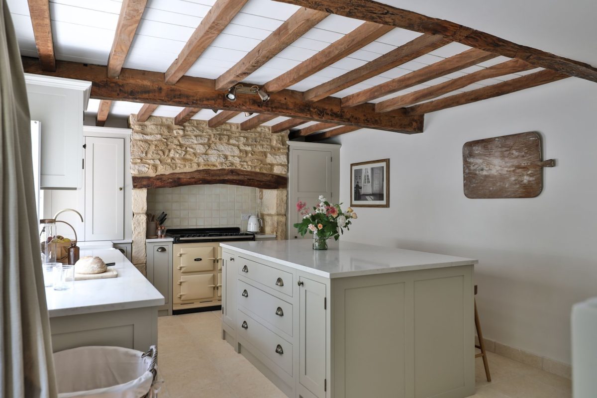 The open-plan kitchen with an island and feature stone wall at Rambling Rose Cottage, Cotswolds