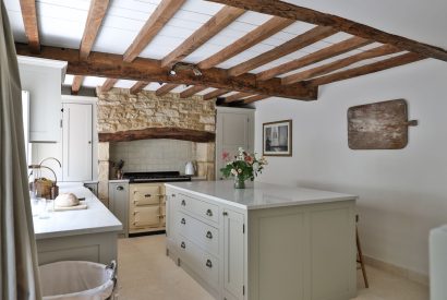 The open-plan kitchen with an island and feature stone wall at Rambling Rose Cottage, Cotswolds