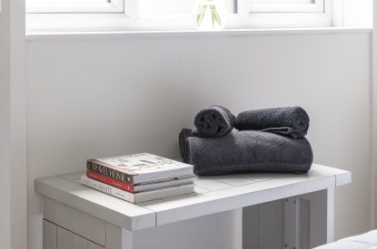 A bedside table with a stack of books and towels at Farmyard Cottage, Wiltshire