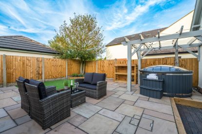 The enclosed garden with a rattan furniture set and a wood-fired hot tub at Pilgrim Cottage, Cheshire