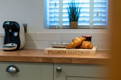 The kitchen counter with a coffee machine and croissants on the chopping board at Pilgrim Cottage, Cheshire