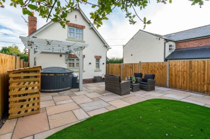 The enclosed garden with an artificial lawn, a rattan furniture set and a wood-fired hot tub at Pilgrim Cottage, Cheshire