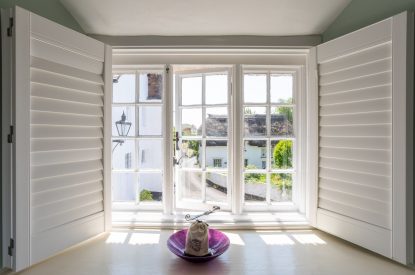 A window with shutters overlooking the quaint village at Thatch Corner, Somerset