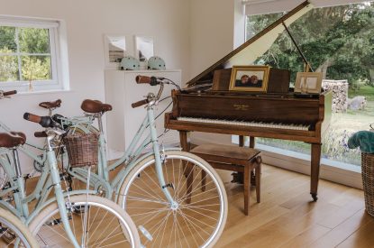 A social space with a grand piano and two bikes overlooking the garden at Brickworks and Vines, Isle of Wight
