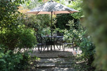 A dining table and parasol in the garden at Rambling Rose Cottage, Cotswolds 